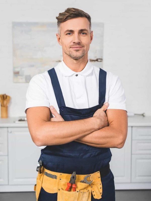 adult-repairman-in-tool-belt-standing-with-crossed-arms-at-kitchen-and-looking-at-camera.jpg