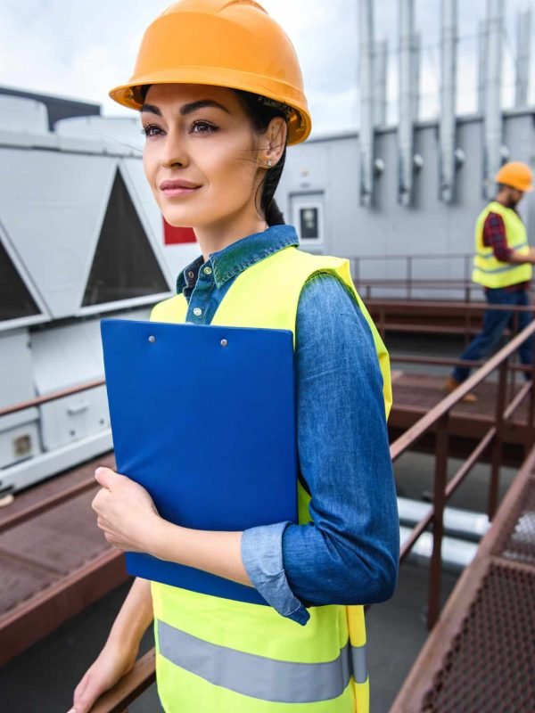 female-architect-in-helmet-holding-clipboard-on-roof-male-colleague-behind.jpg